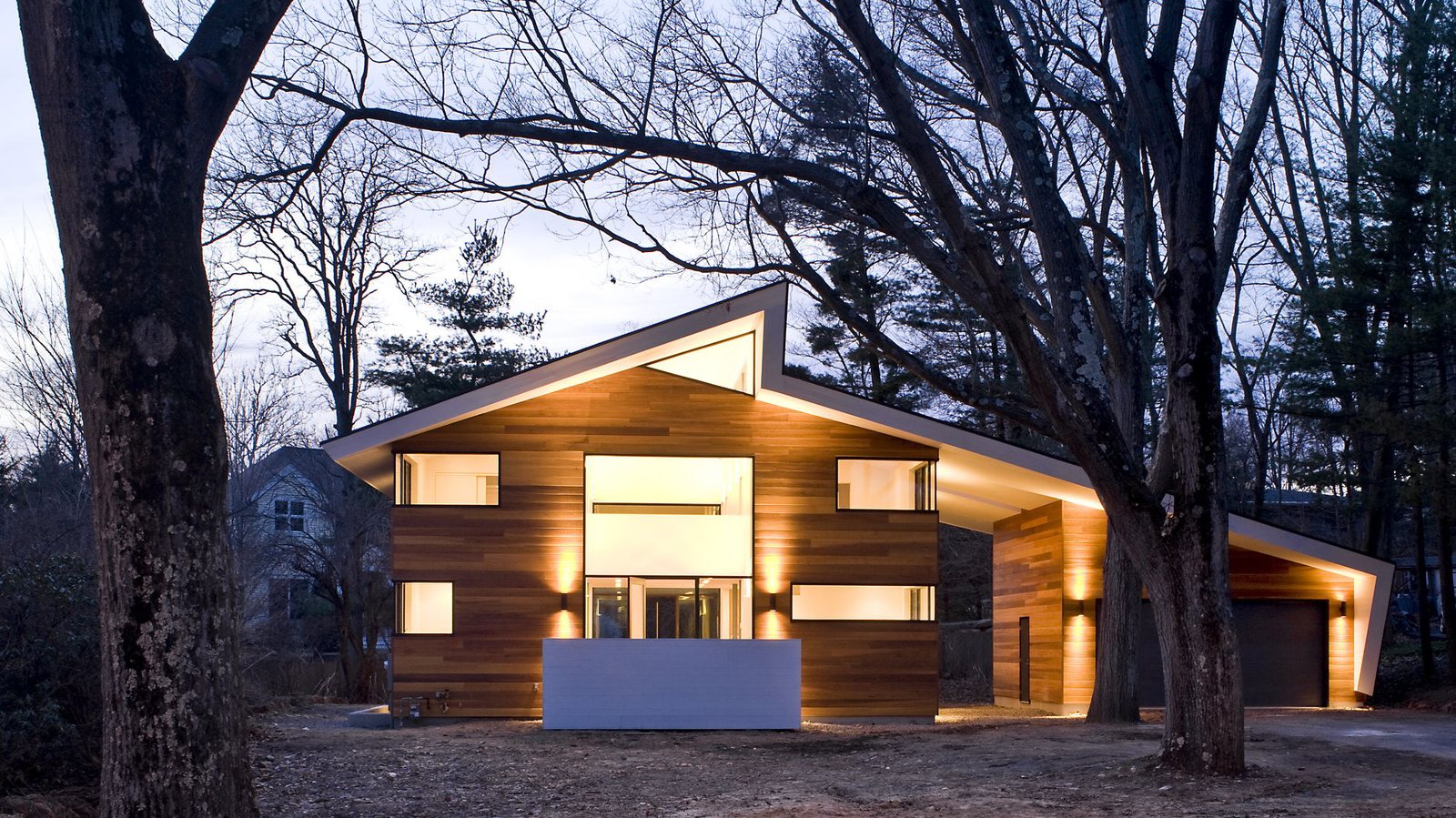 Gallery House at dusk, a cedar-clad house with a monumental folded roof, lit from within